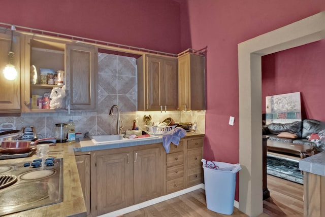 kitchen with backsplash, sink, stovetop, and light wood-type flooring