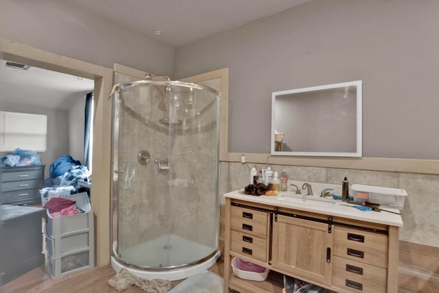 bathroom with vanity, wood-type flooring, a shower with door, and tile walls