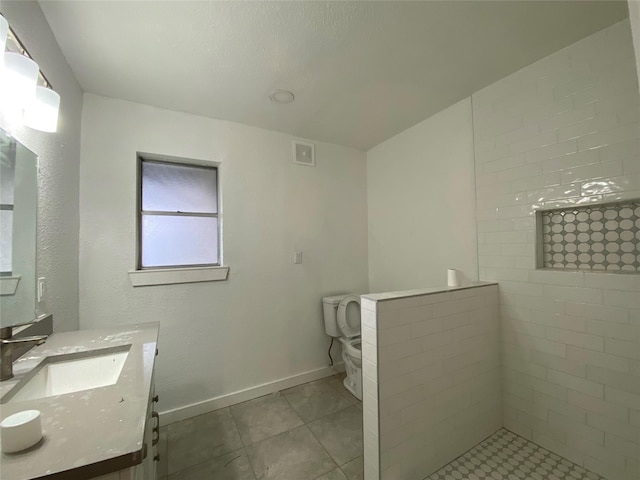 bathroom with a tile shower, vanity, and toilet