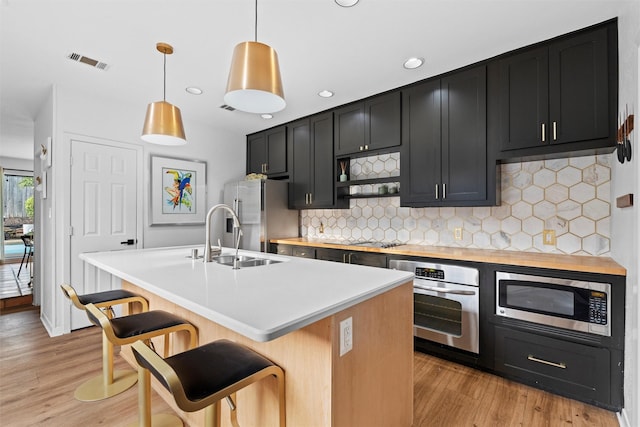 kitchen with pendant lighting, a center island with sink, tasteful backsplash, a kitchen bar, and stainless steel appliances