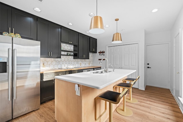 kitchen featuring stainless steel refrigerator with ice dispenser, a breakfast bar, sink, hanging light fixtures, and an island with sink