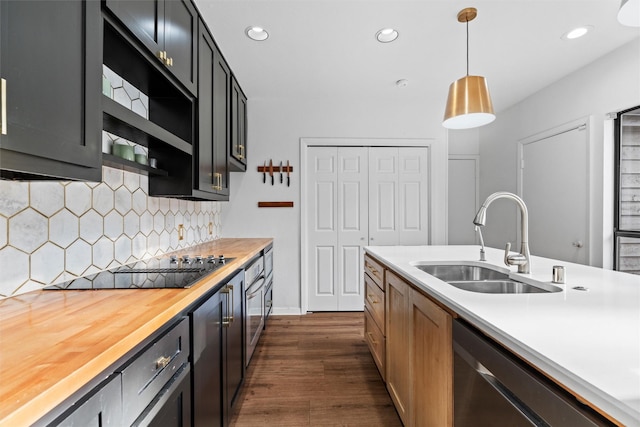 kitchen featuring backsplash, stainless steel dishwasher, sink, decorative light fixtures, and butcher block countertops