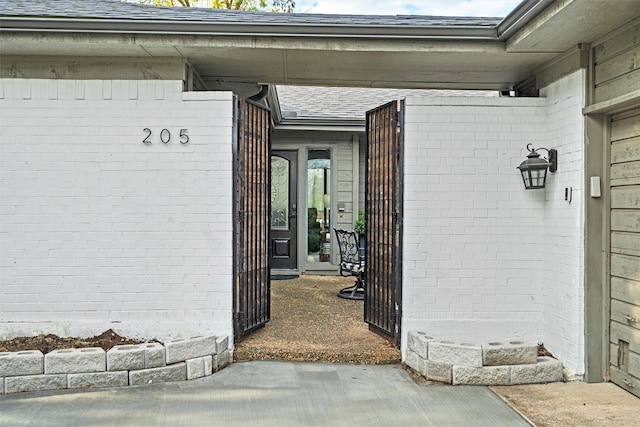 view of exterior entry featuring a shingled roof and brick siding