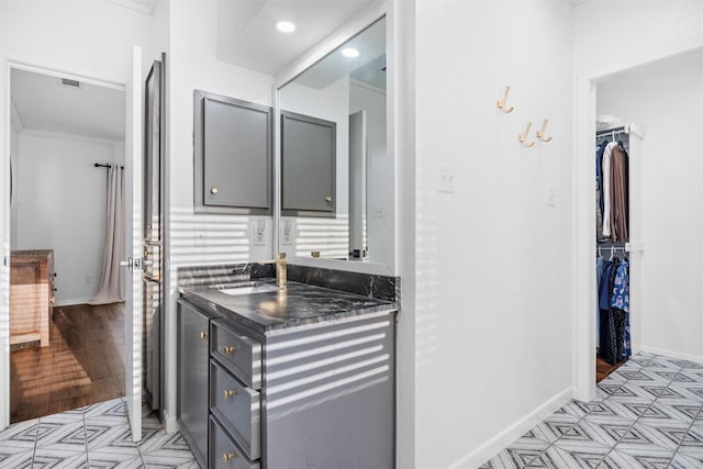 bathroom featuring a walk in closet, vanity, baseboards, visible vents, and crown molding