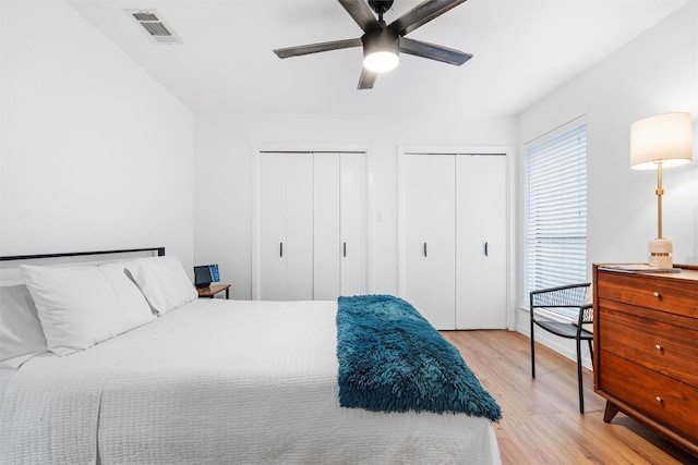 bedroom with ceiling fan, visible vents, multiple closets, and light wood finished floors