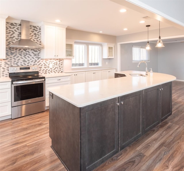 kitchen with electric stove, sink, wall chimney exhaust hood, and an island with sink