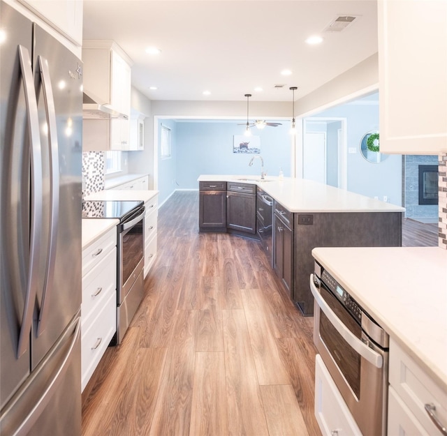 kitchen with appliances with stainless steel finishes, white cabinetry, hanging light fixtures, dark brown cabinetry, and light wood-type flooring