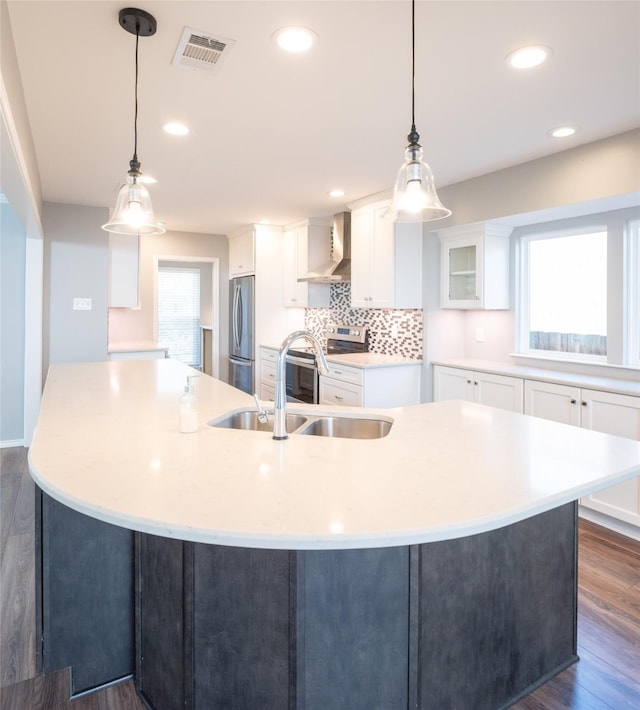 kitchen with wall chimney exhaust hood, stainless steel appliances, hanging light fixtures, and a large island with sink