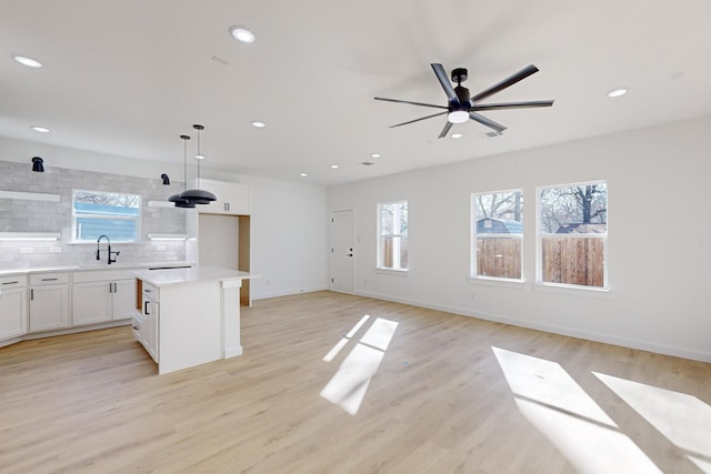 kitchen with white cabinets, light wood-type flooring, decorative light fixtures, and a kitchen island