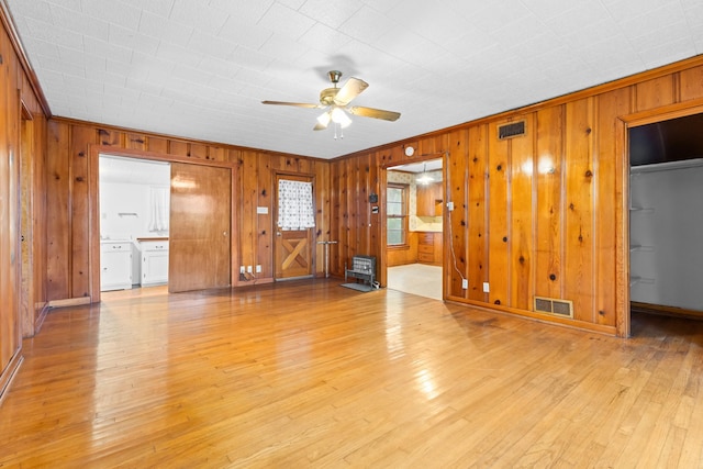 interior space with ceiling fan, light hardwood / wood-style floors, and wood walls