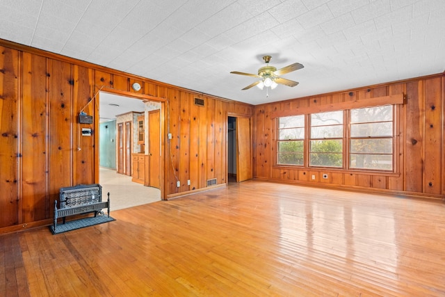 unfurnished living room with ceiling fan, wooden walls, and light wood-type flooring