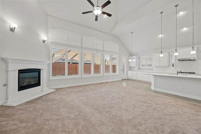 unfurnished living room with light carpet, sink, ceiling fan, and high vaulted ceiling