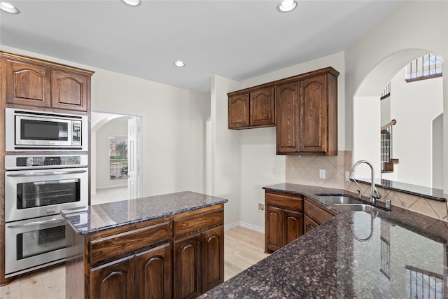 kitchen with sink, dark stone countertops, appliances with stainless steel finishes, tasteful backsplash, and light hardwood / wood-style floors