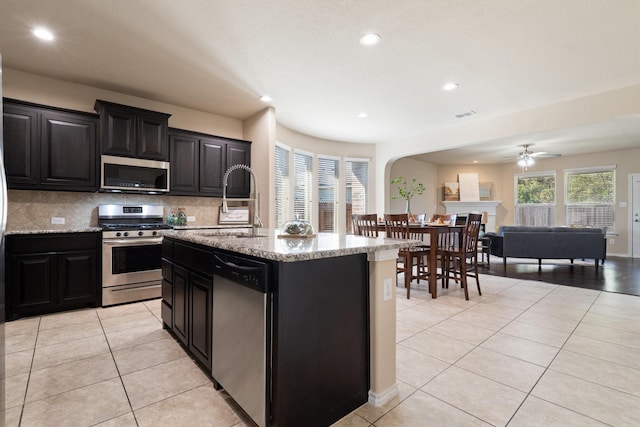 kitchen featuring light tile patterned flooring, stainless steel appliances, tasteful backsplash, and an island with sink