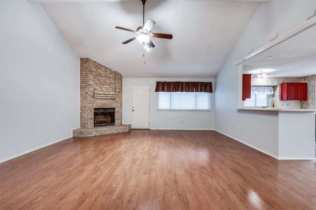 unfurnished living room featuring ceiling fan, a fireplace, lofted ceiling, and light hardwood / wood-style flooring