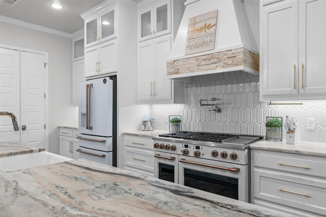 kitchen with white cabinetry, premium appliances, premium range hood, backsplash, and ornamental molding