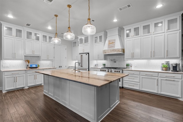 kitchen featuring premium range hood, a center island with sink, white cabinets, and decorative light fixtures