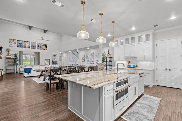 kitchen featuring lofted ceiling with beams, decorative light fixtures, a kitchen island with sink, and white cabinets