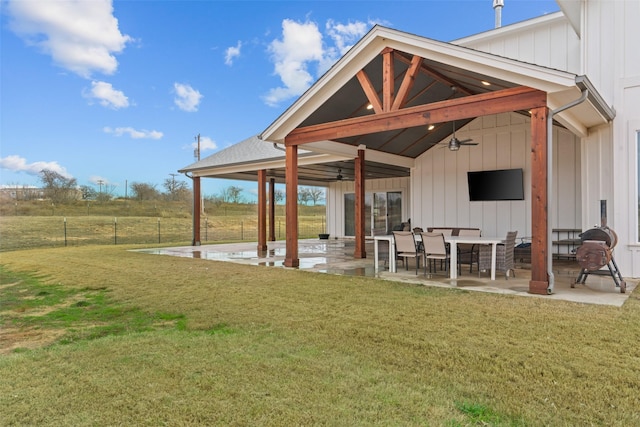 back of property with a rural view, ceiling fan, a patio area, and a lawn