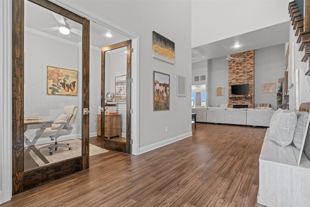 living room with a stone fireplace, hardwood / wood-style floors, a high ceiling, ceiling fan, and crown molding