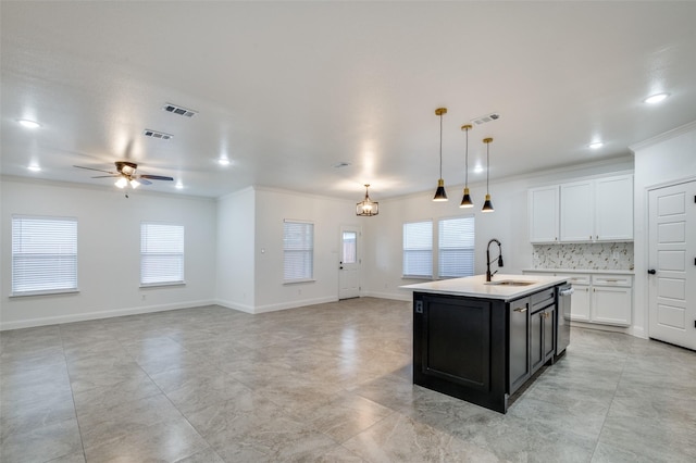 kitchen featuring decorative light fixtures, tasteful backsplash, sink, white cabinets, and a center island with sink