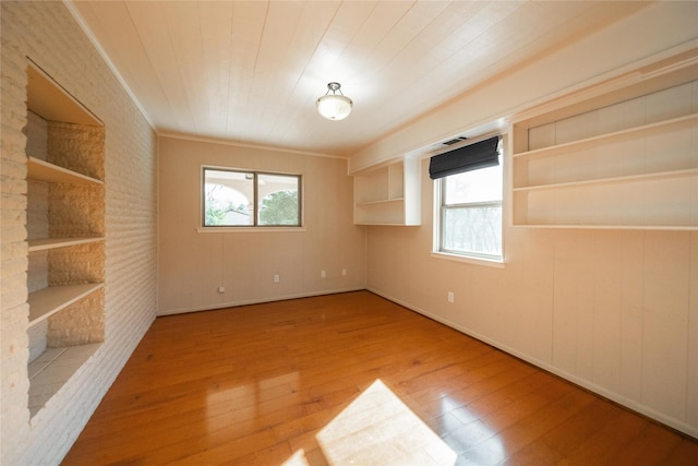 unfurnished room with built in shelves, ornamental molding, and light hardwood / wood-style flooring