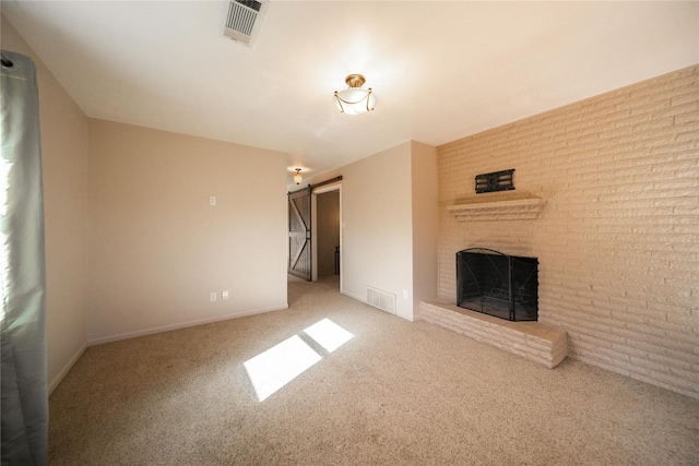 unfurnished living room with carpet, a barn door, and a brick fireplace