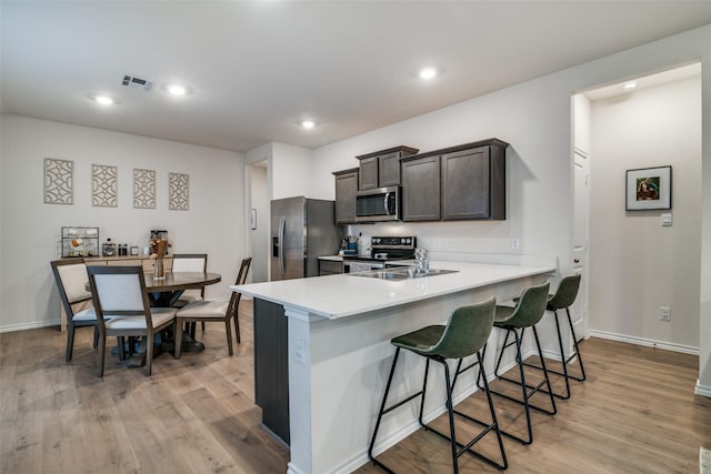 kitchen with sink, a breakfast bar area, light hardwood / wood-style flooring, kitchen peninsula, and stainless steel appliances