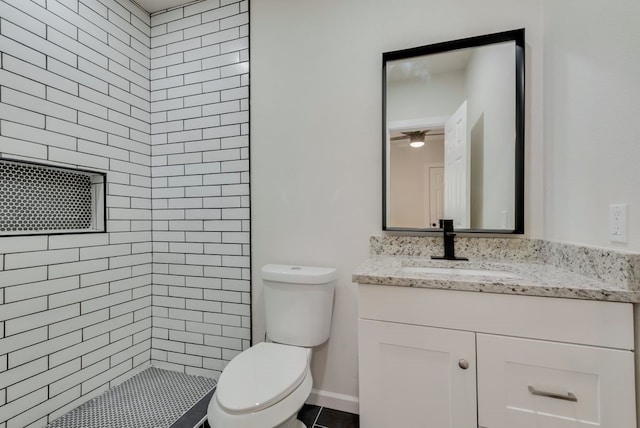 bathroom with a tile shower, vanity, and toilet