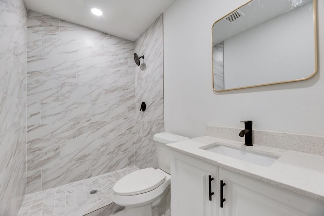 bathroom featuring a tile shower, vanity, and toilet