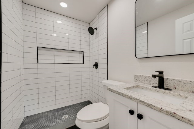 bathroom with a tile shower, vanity, and toilet