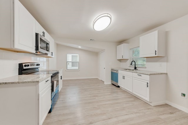 kitchen with light stone countertops, sink, lofted ceiling, white cabinets, and appliances with stainless steel finishes