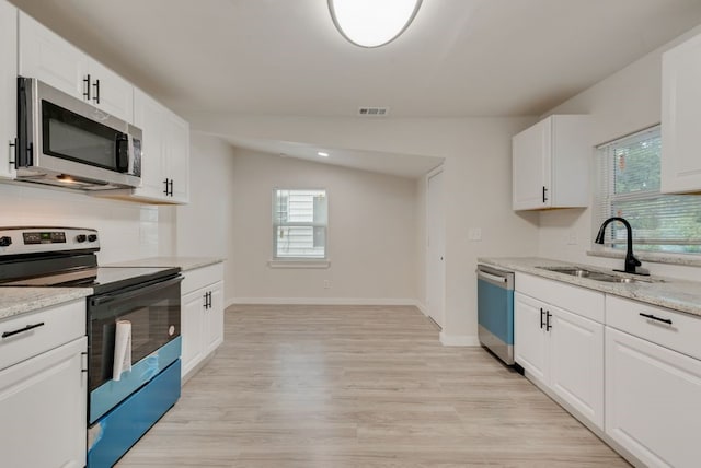 kitchen featuring lofted ceiling, white cabinets, sink, light stone countertops, and appliances with stainless steel finishes