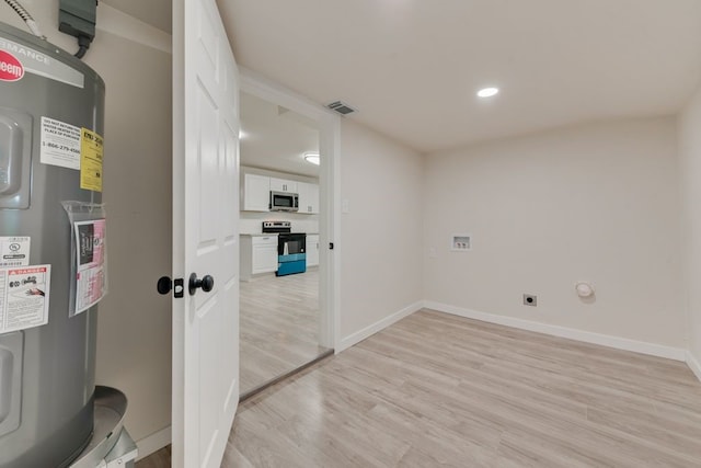 clothes washing area with electric water heater and light hardwood / wood-style floors