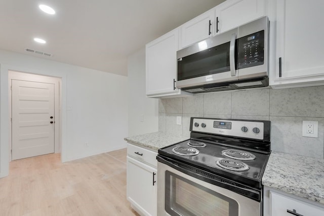 kitchen with white cabinets, light hardwood / wood-style flooring, light stone countertops, appliances with stainless steel finishes, and tasteful backsplash