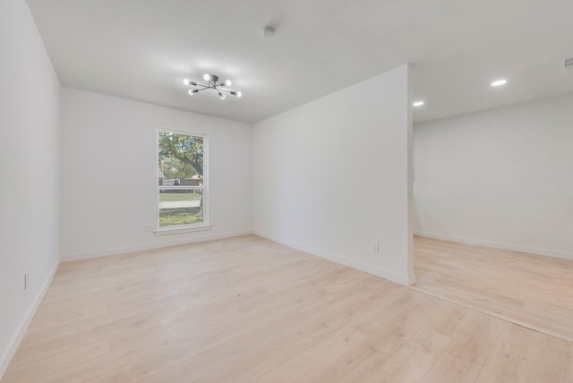 empty room featuring a notable chandelier and light hardwood / wood-style floors