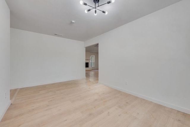 spare room with a chandelier and light wood-type flooring