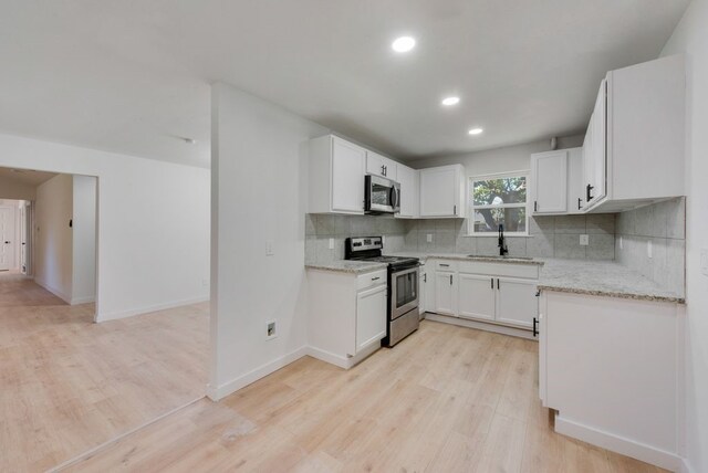 kitchen featuring appliances with stainless steel finishes, backsplash, light wood-type flooring, sink, and white cabinets