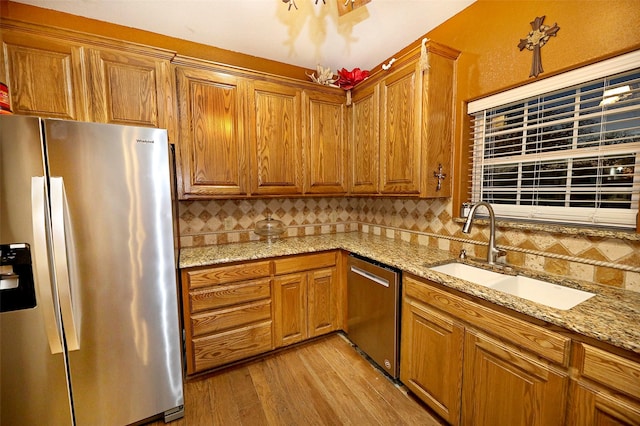 kitchen featuring sink, stainless steel appliances, light stone counters, backsplash, and light hardwood / wood-style floors