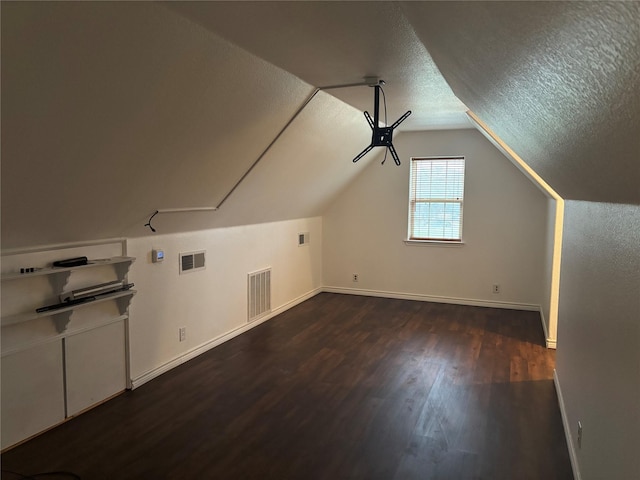 bonus room with vaulted ceiling, dark wood-type flooring, and a textured ceiling