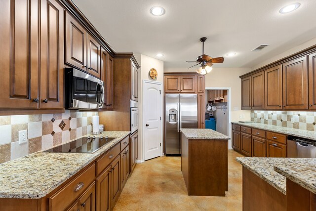 kitchen featuring tasteful backsplash, light stone countertops, a kitchen island, and appliances with stainless steel finishes