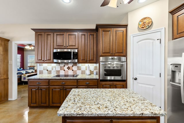 kitchen with ceiling fan, light stone counters, decorative backsplash, a kitchen island, and appliances with stainless steel finishes