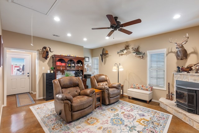 living room featuring a wood stove, ceiling fan, and concrete flooring