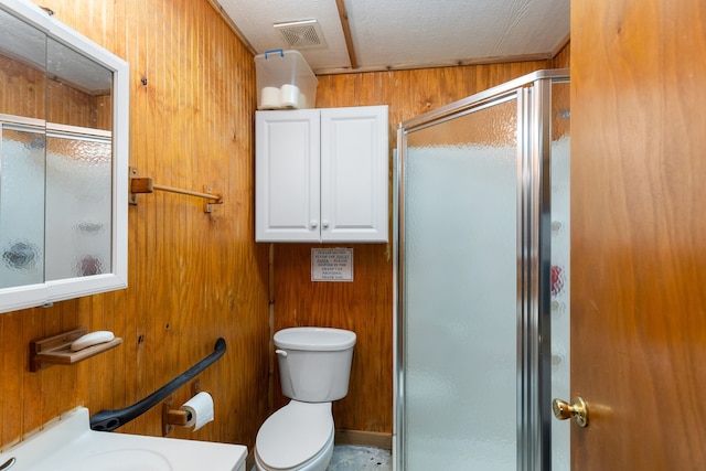 bathroom with vanity, wood walls, toilet, a textured ceiling, and a shower with shower door