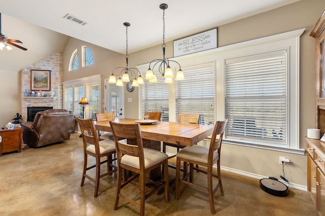 dining space with ceiling fan with notable chandelier, lofted ceiling, and a fireplace