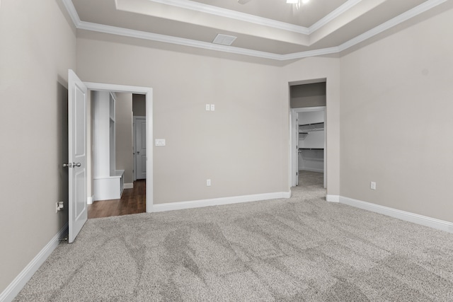 unfurnished bedroom with crown molding, a tray ceiling, a walk in closet, and carpet