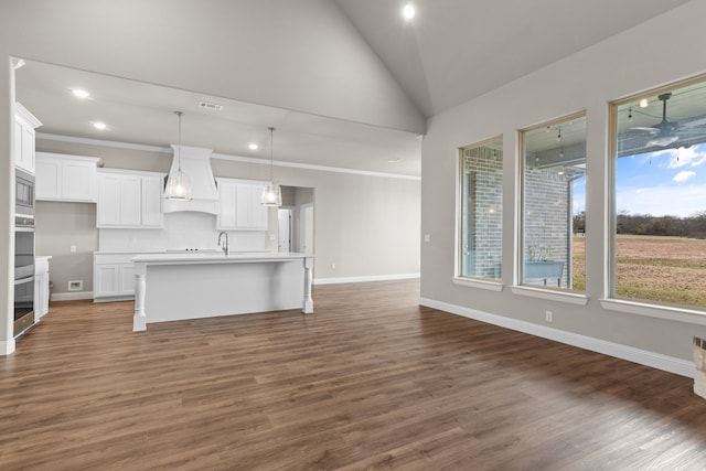 kitchen featuring a kitchen island with sink, decorative light fixtures, custom exhaust hood, and white cabinets