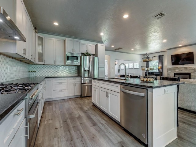 kitchen with sink, wall chimney exhaust hood, stainless steel appliances, a fireplace, and white cabinets