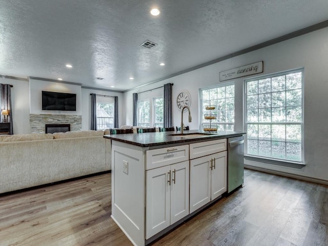 kitchen featuring white cabinets, a center island with sink, sink, light wood-type flooring, and a fireplace