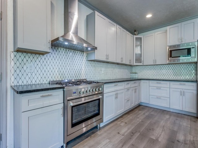 kitchen featuring appliances with stainless steel finishes, tasteful backsplash, wall chimney range hood, light hardwood / wood-style flooring, and white cabinetry